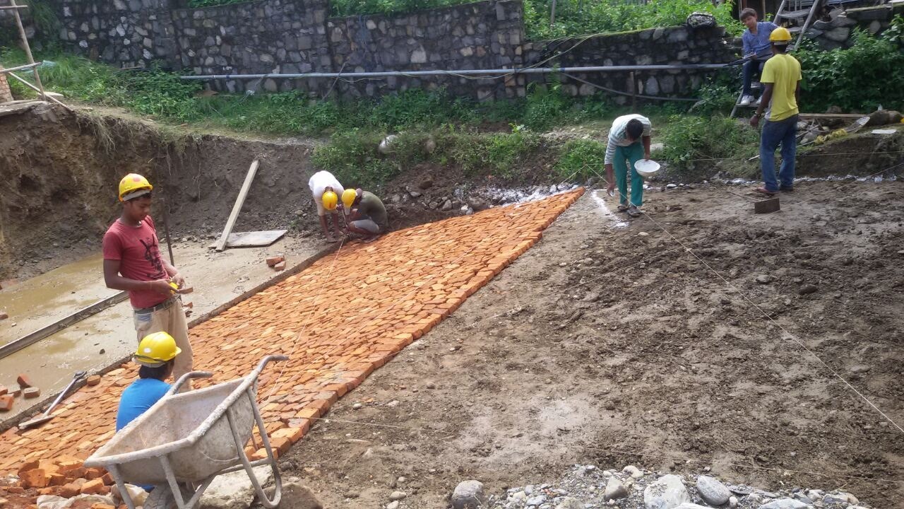 Pool construction stage 1: workers preparing brick bedding inside the excavated pool area.