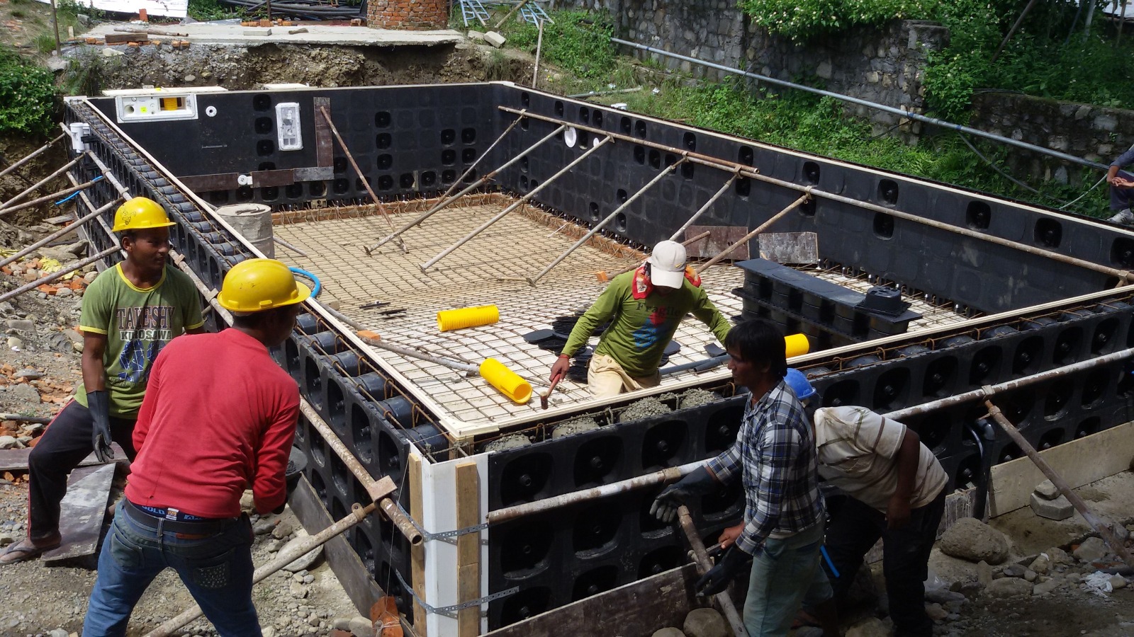 Pool construction stage 4: workers placing concrete into braced pool wall panels beside the reinforced floor.