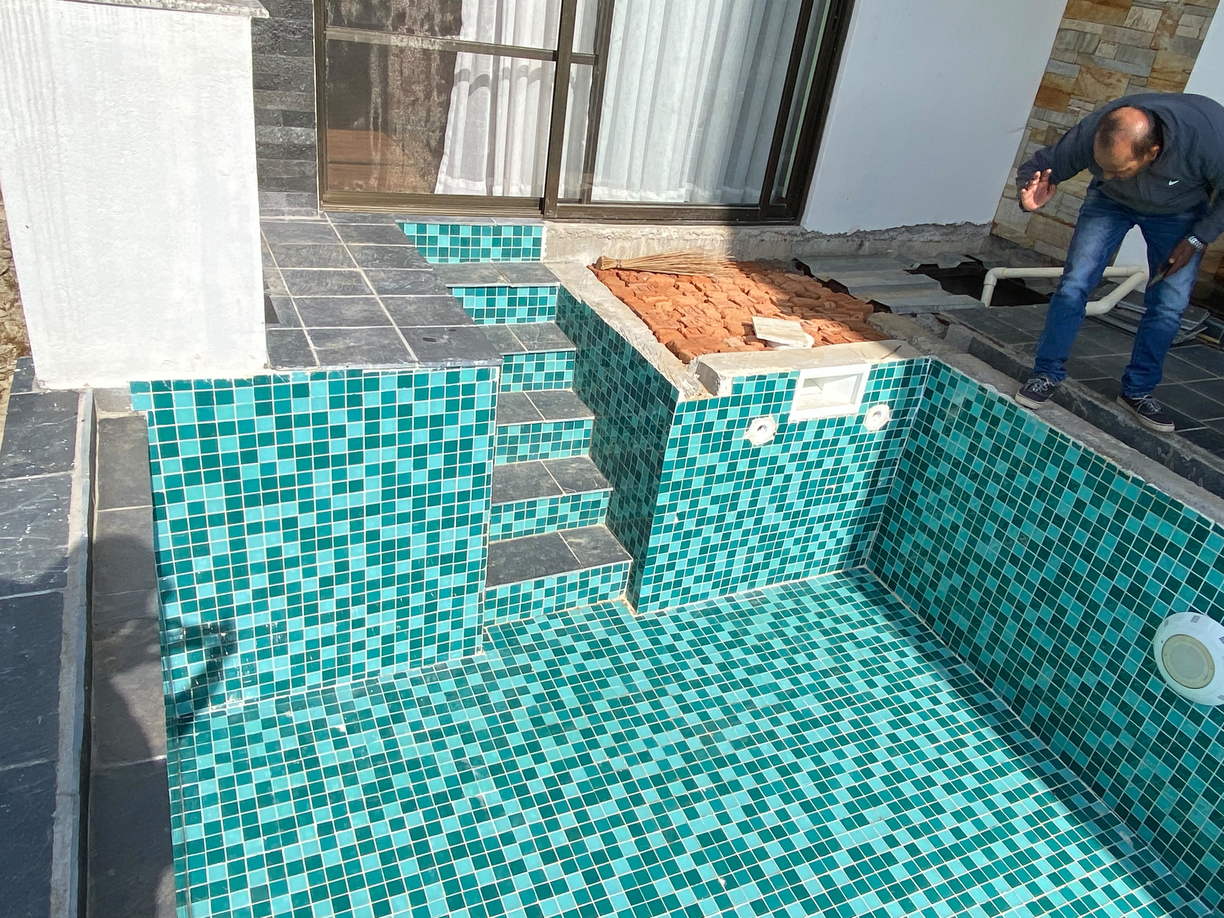 Residential pool during construction in Tokha, showing green mosaic tiles, entry steps and installed pool fittings.