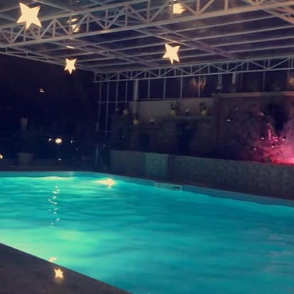 Illuminated covered swimming pool at Legacy Hotel at night, beneath steel roof trusses and star-shaped lights.