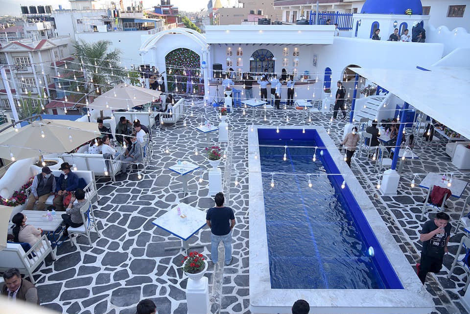 Rooftop pool and stone-patterned terrace at Aema Café in Boudha, with white and blue buildings.
