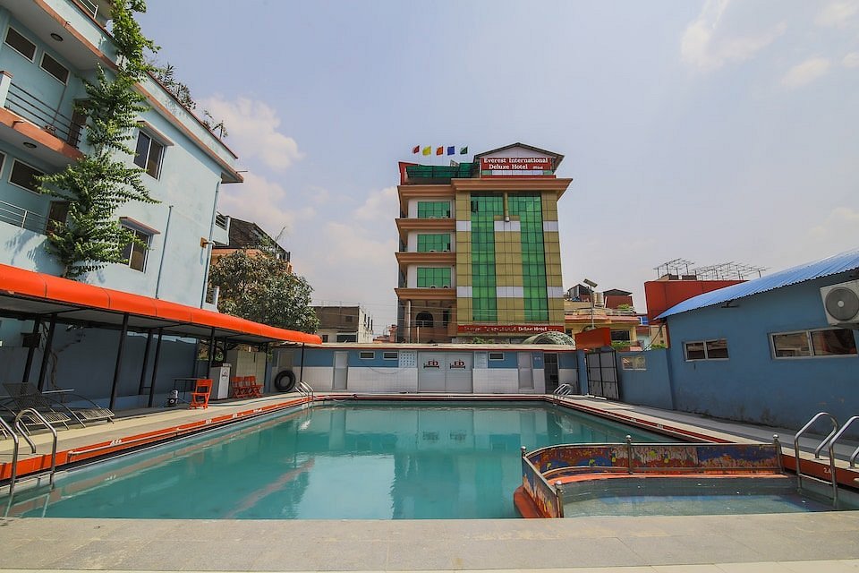 Outdoor swimming pool at Hotel Tulip, with an adjoining smaller pool, pool ladders and a paved deck.